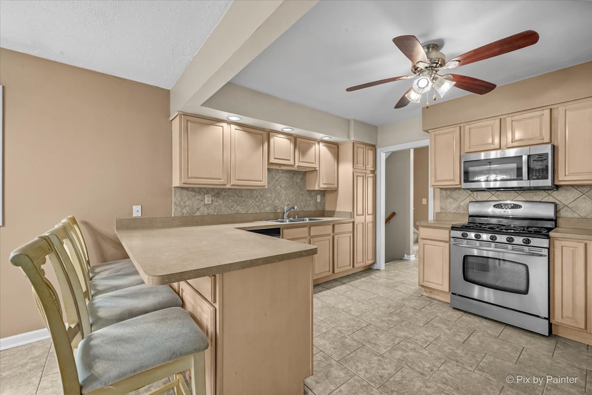 Kitchen with light maple cabinets, a gas range, and a breakfast bar with stools